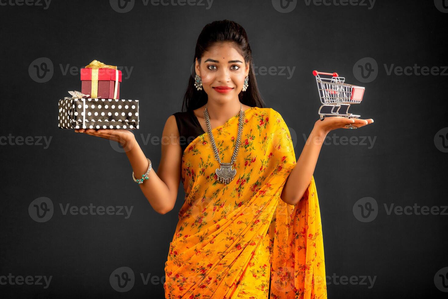 Beautiful young girl or woman holding and posing with a miniature trolley shopping cart and gift box on a gray background photo