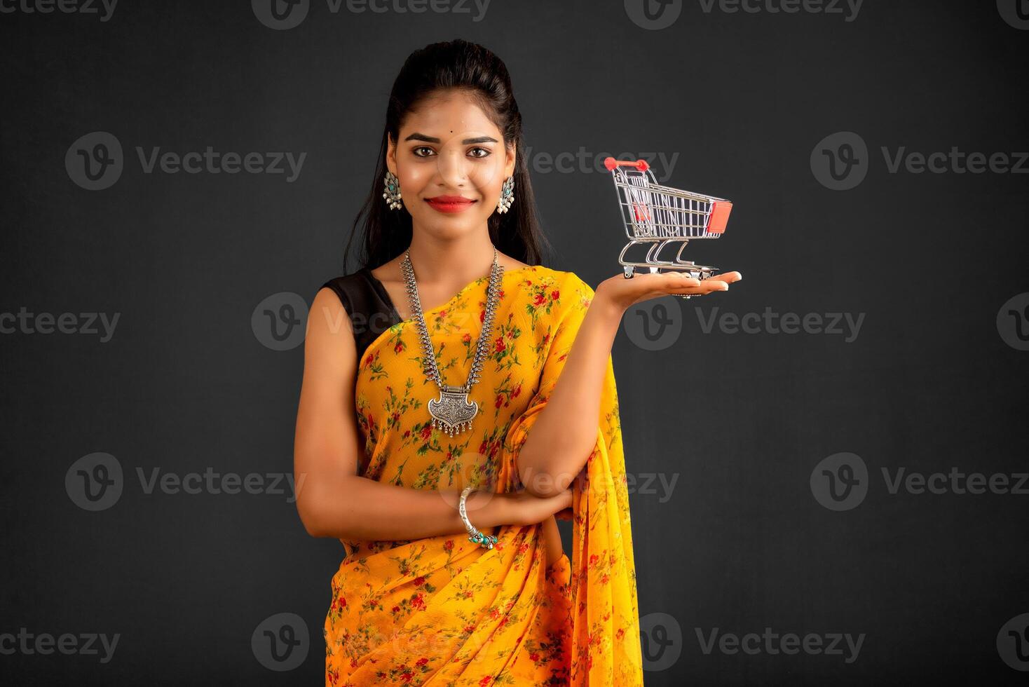 Happy young Smiling girl with a miniature trolley shopping cart on the gray background. Beautiful girl in shopping concept. photo