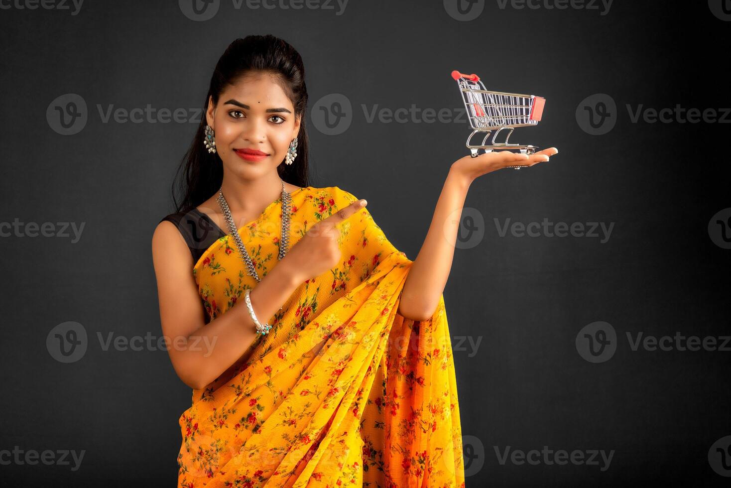 Happy young Smiling girl with a miniature trolley shopping cart on the gray background. Beautiful girl in shopping concept. photo
