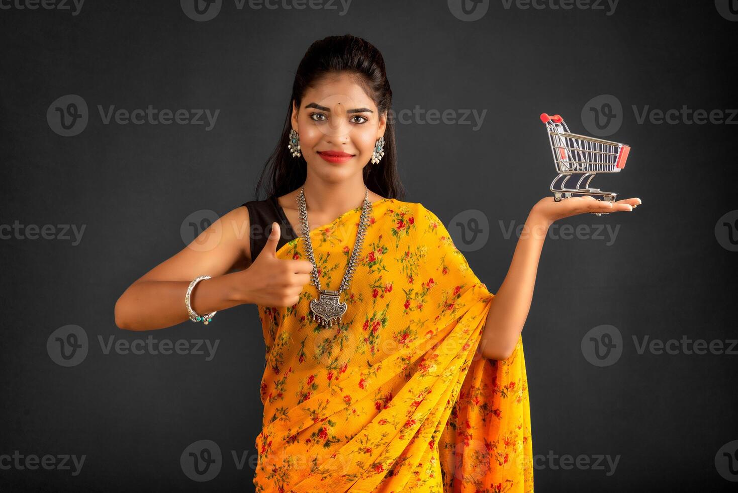 Happy young Smiling girl with a miniature trolley shopping cart on the gray background. Beautiful girl in shopping concept. photo