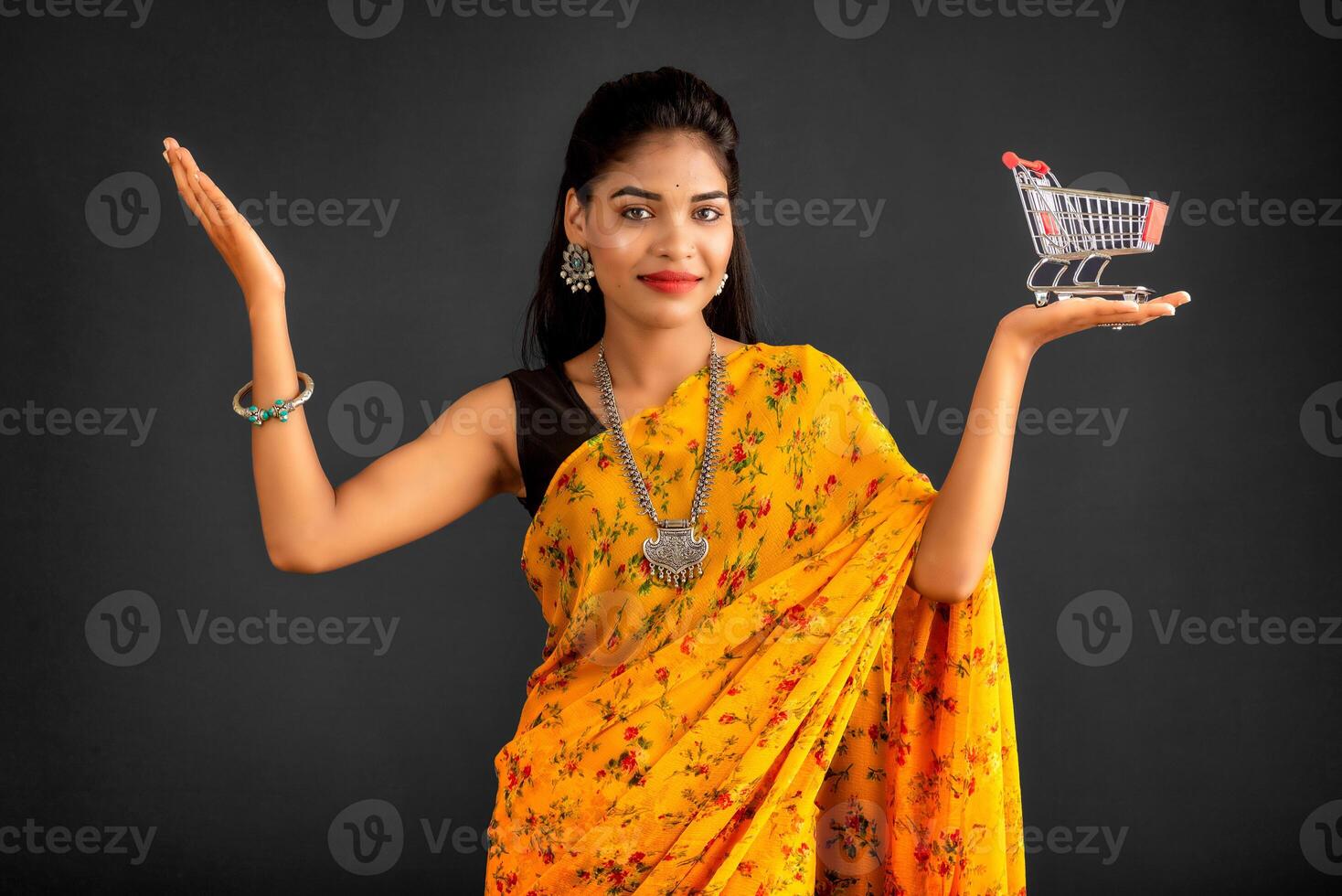 Happy young Smiling girl with a miniature trolley shopping cart on the gray background. Beautiful girl in shopping concept. photo