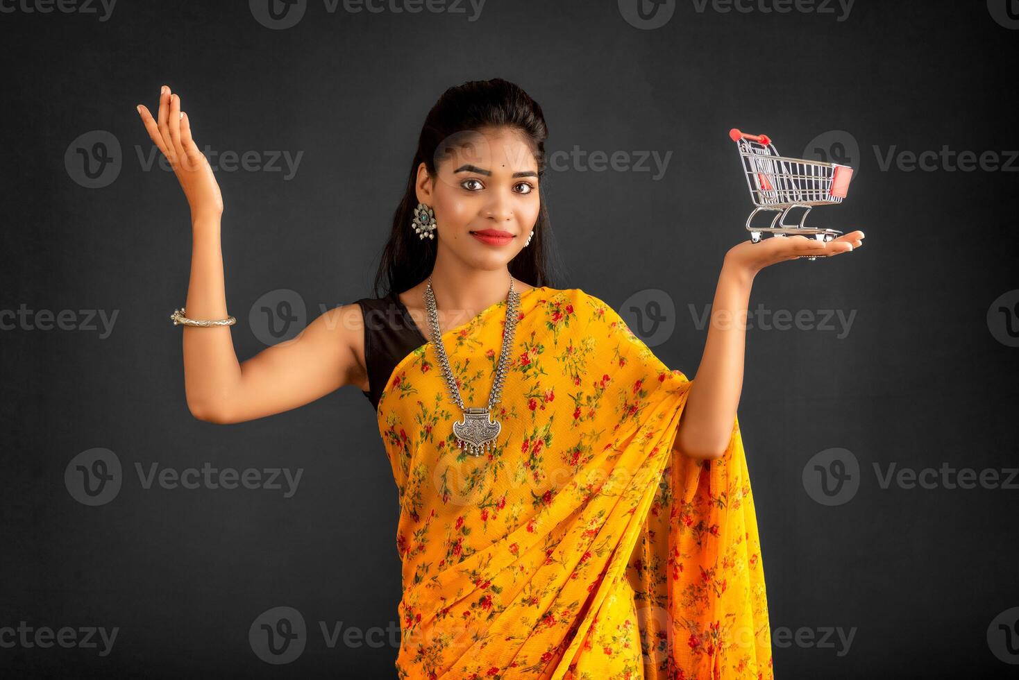 Happy young Smiling girl with a miniature trolley shopping cart on the gray background. Beautiful girl in shopping concept. photo
