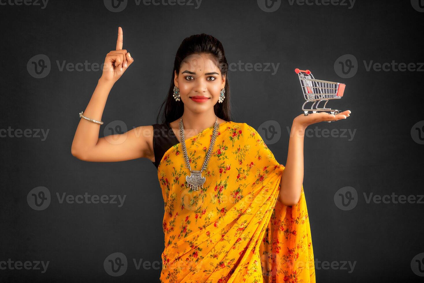 Happy young Smiling girl with a miniature trolley shopping cart on the gray background. Beautiful girl in shopping concept. photo