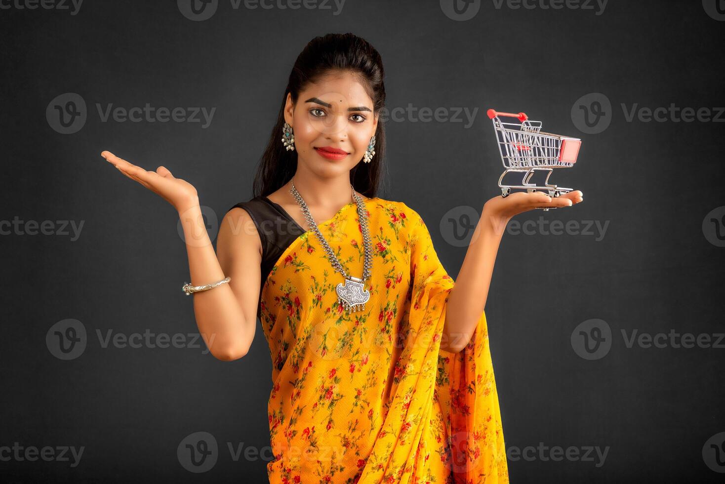 Happy young Smiling girl with a miniature trolley shopping cart on the gray background. Beautiful girl in shopping concept. photo