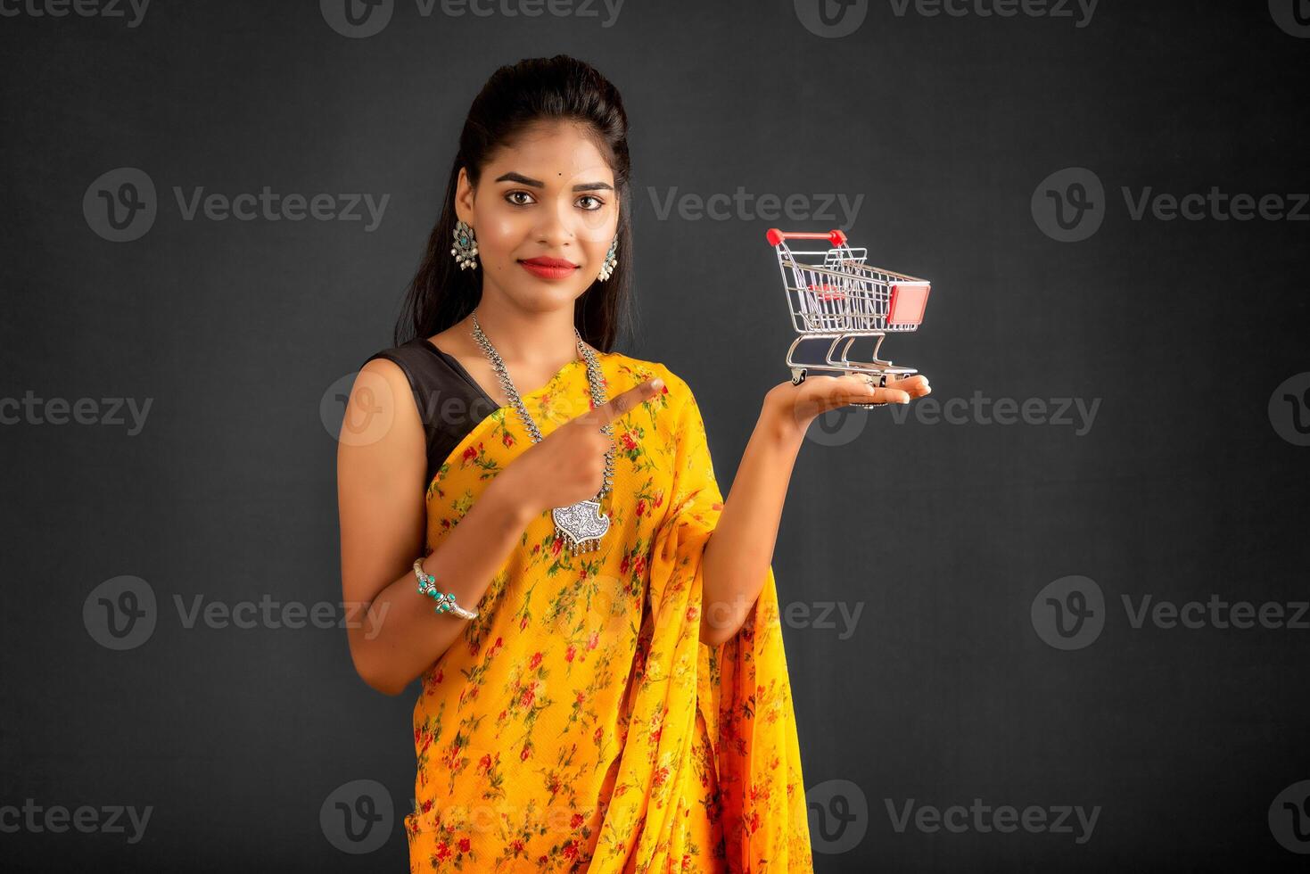 Happy young Smiling girl with a miniature trolley shopping cart on the gray background. Beautiful girl in shopping concept. photo