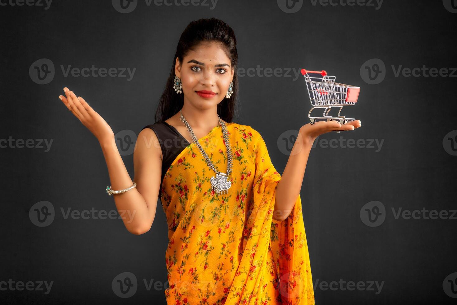 Happy young Smiling girl with a miniature trolley shopping cart on the gray background. Beautiful girl in shopping concept. photo