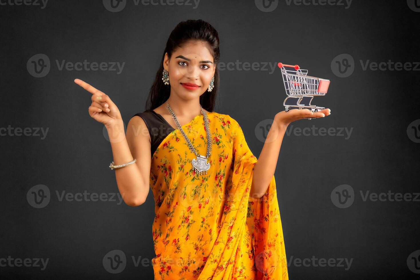 Happy young Smiling girl with a miniature trolley shopping cart on the gray background. Beautiful girl in shopping concept. photo