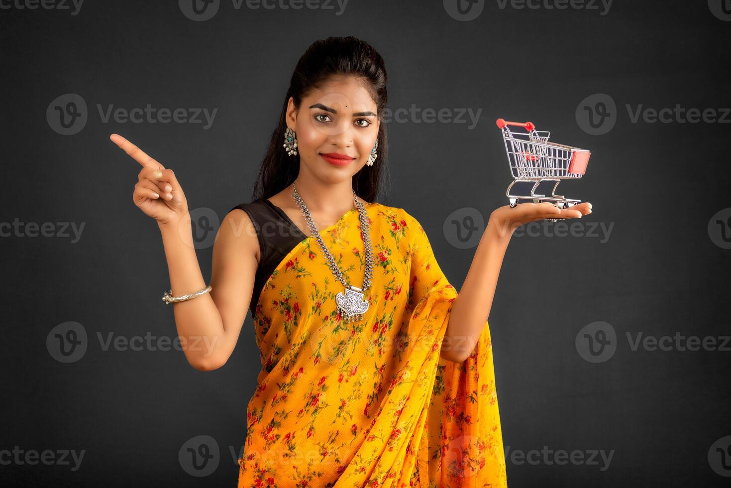 Happy young Smiling girl with a miniature trolley shopping cart on the gray background. Beautiful girl in shopping concept. photo