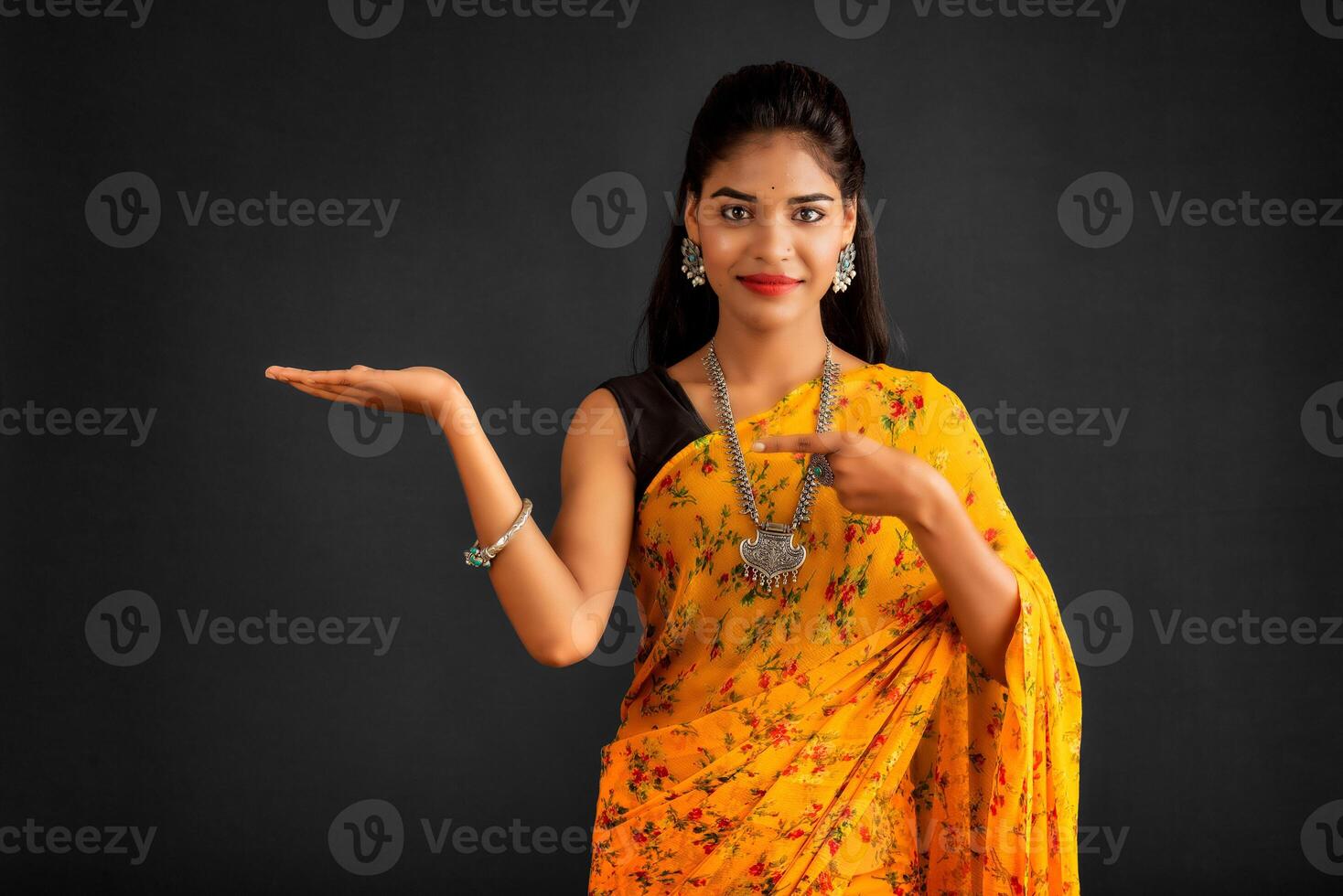 Portrait of a successful cheerful young girl holding and presenting something on hand with a happy smiling face. photo