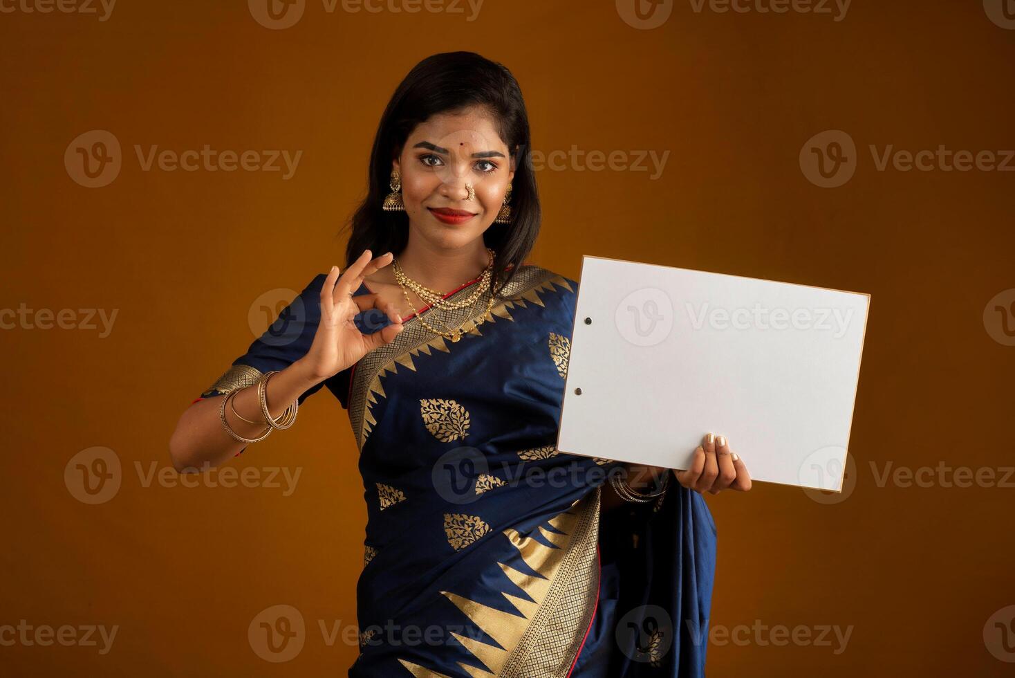A young Indian girl or woman holding a signboard in her hands on a brown background. photo