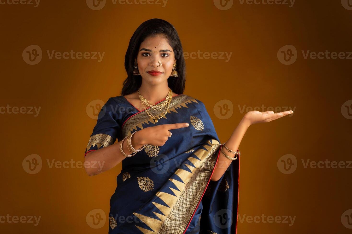 Portrait of Indian traditional young woman or girl presenting something, showing copy space on her palm on a brown background photo