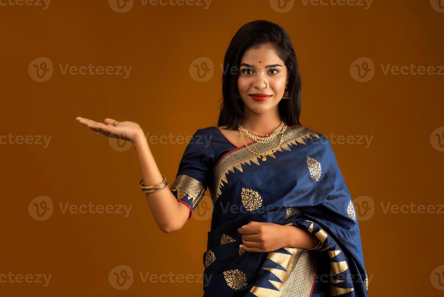 Portrait of Indian traditional young woman or girl presenting something, showing copy space on her palm on a brown background photo