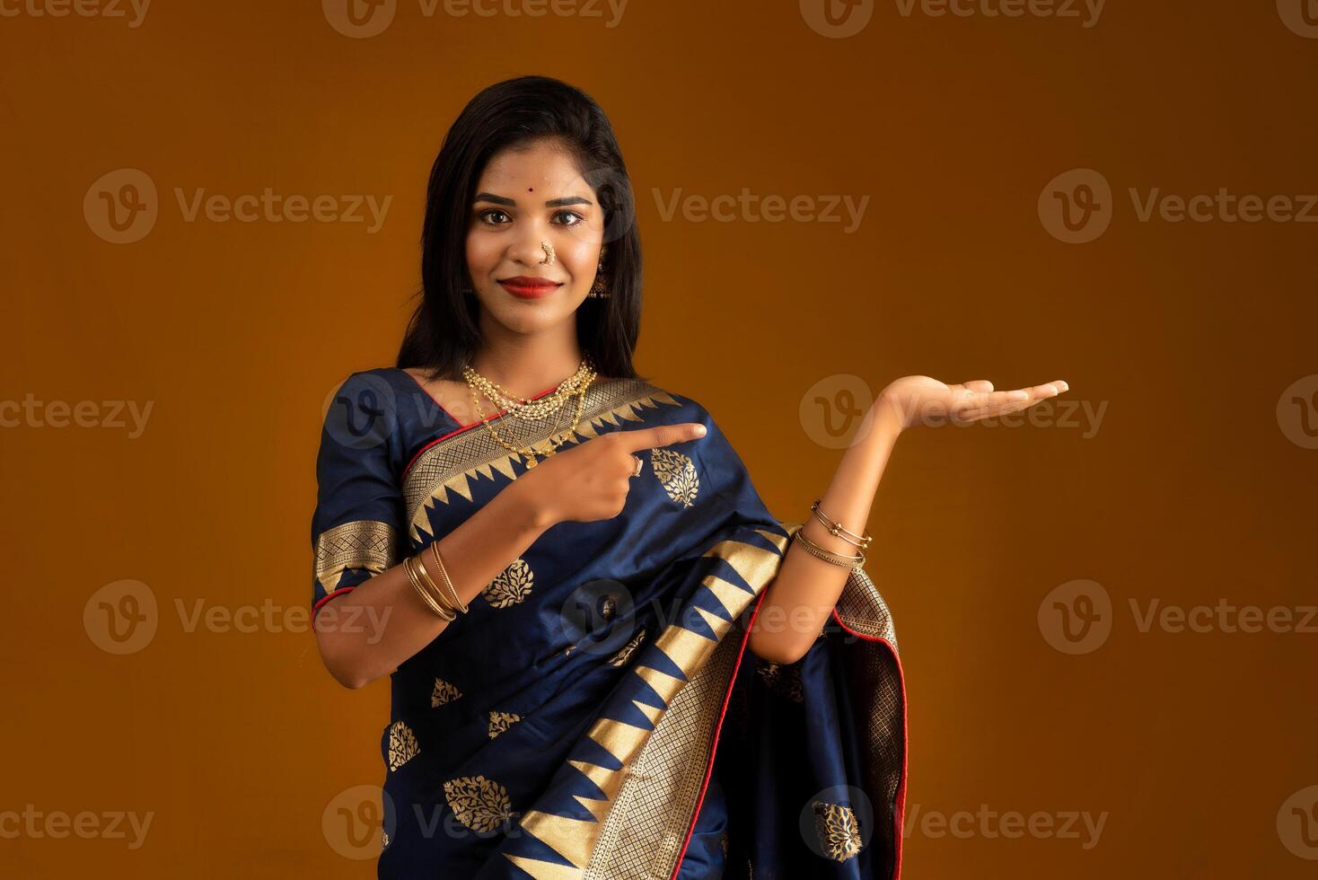 Portrait of Indian traditional young woman or girl presenting something, showing copy space on her palm on a brown background photo