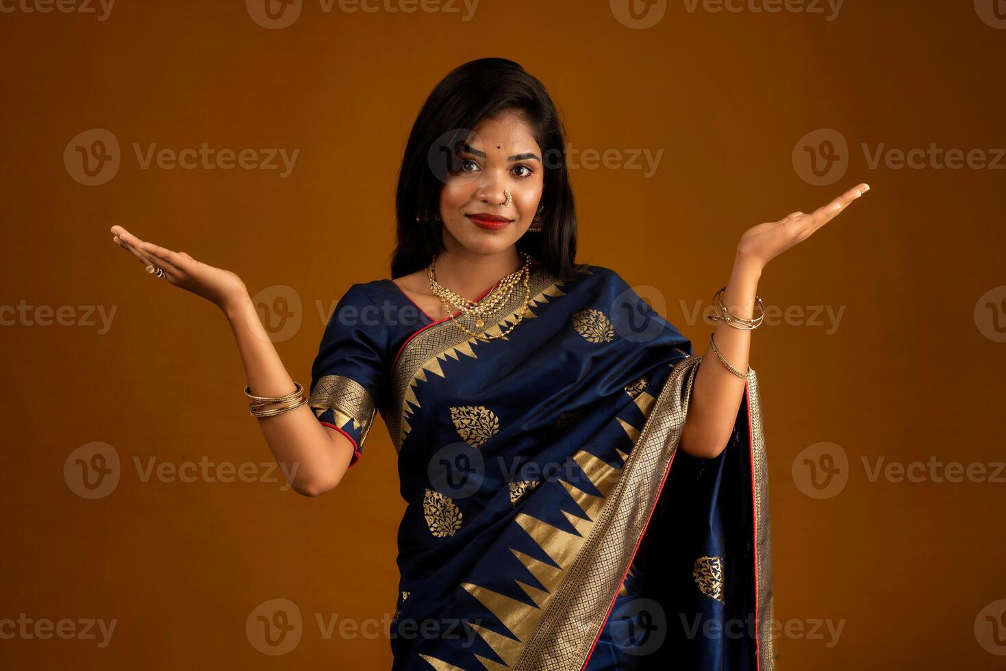 Portrait of Indian traditional young woman or girl presenting something, showing copy space on her palm on a brown background photo
