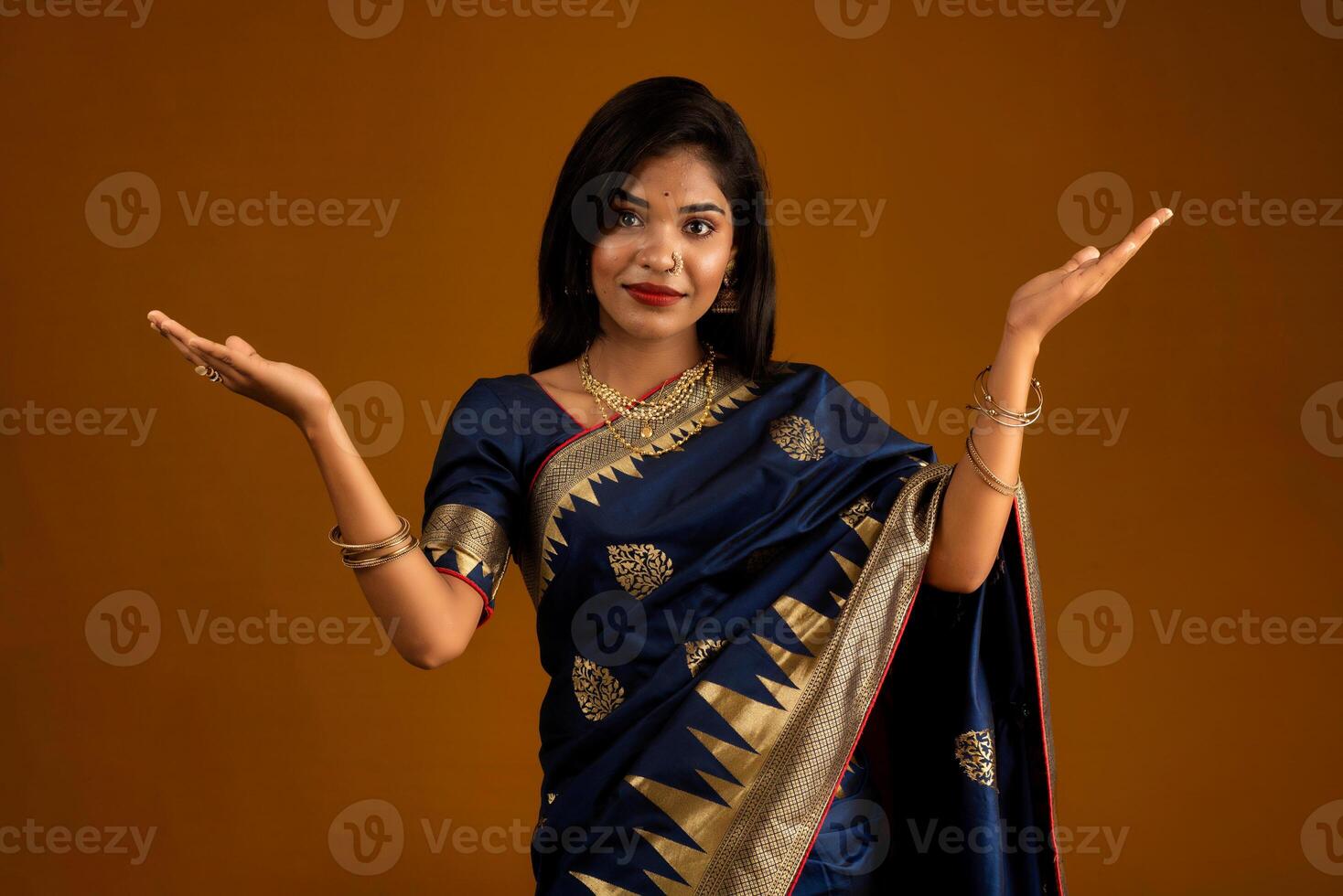 Portrait of Indian traditional young woman or girl presenting something, showing copy space on her palm on a brown background photo