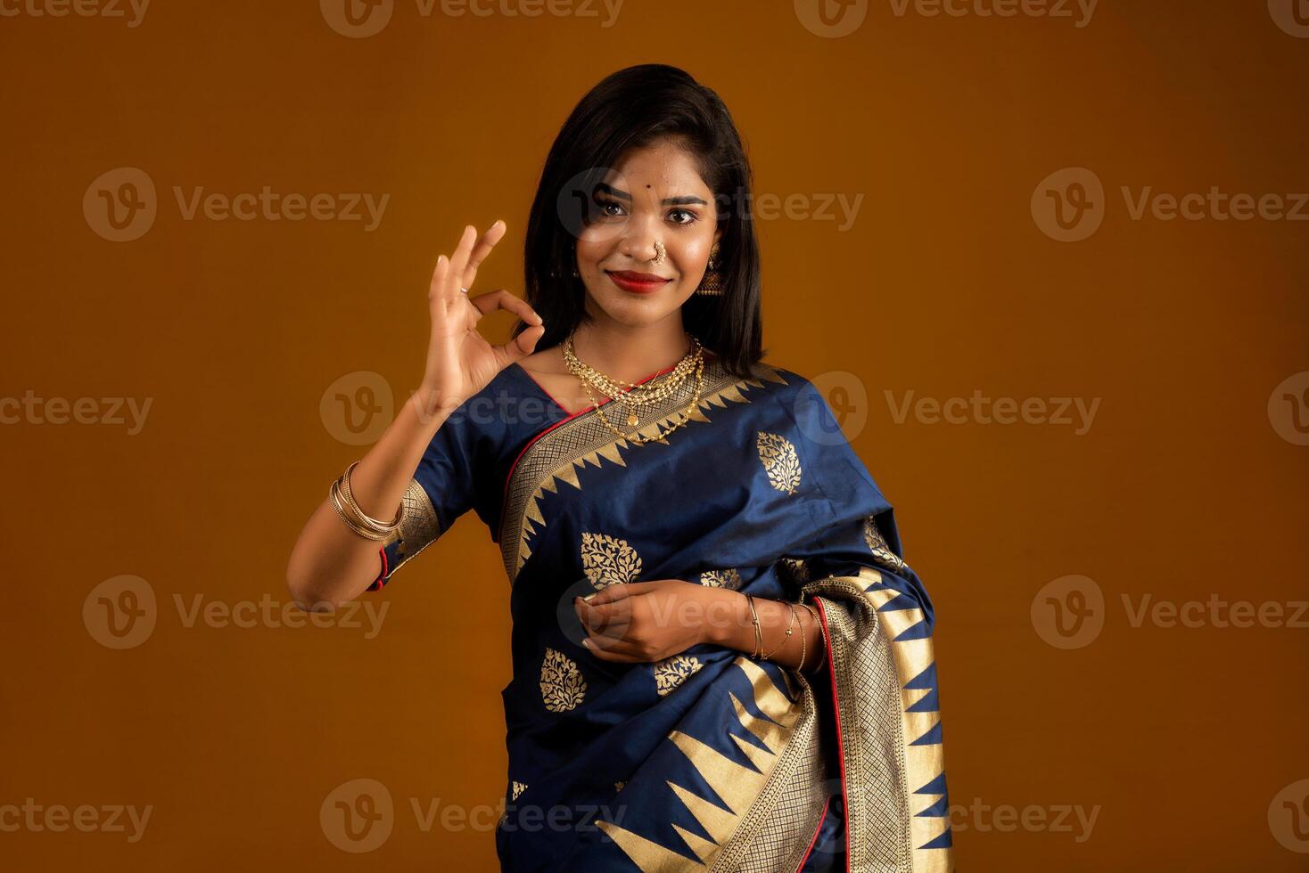 Young smiling girl showing ok sign on a brown background photo