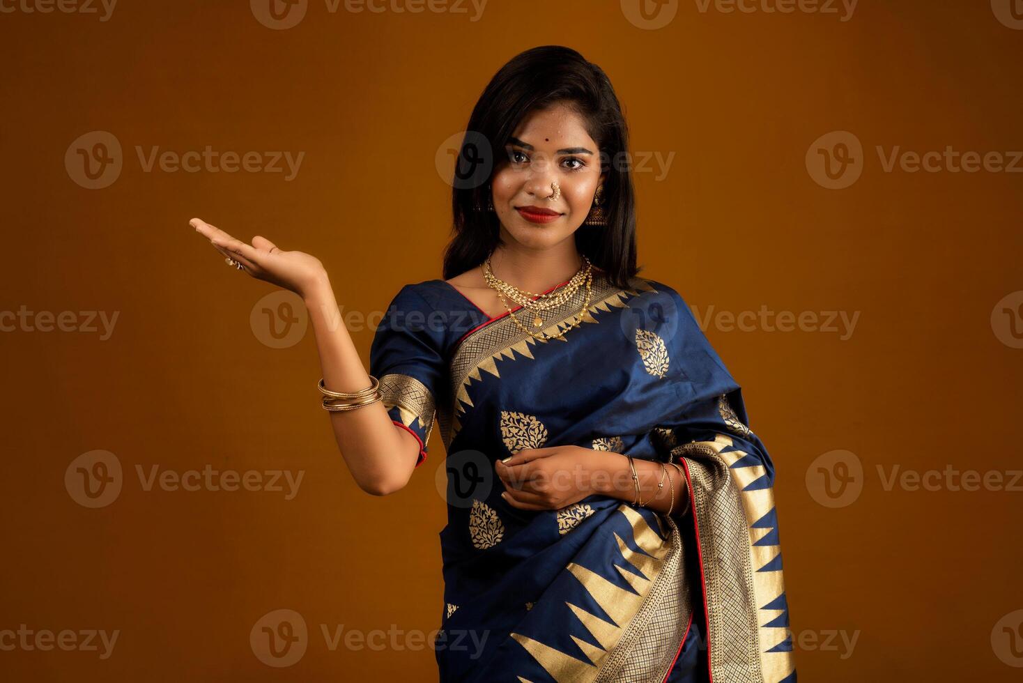 Portrait of Indian traditional young woman or girl presenting something, showing copy space on her palm on a brown background photo
