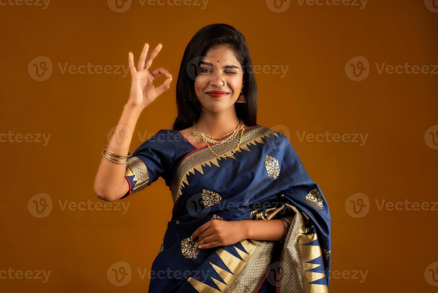Young smiling girl showing ok sign on a brown background photo