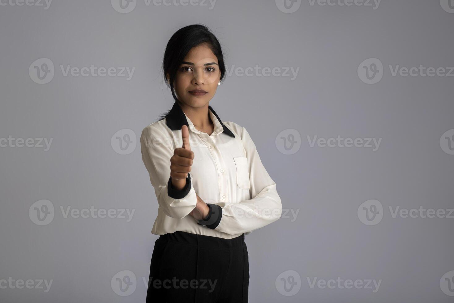 Young smiling girl showing ok sign or thumbs up on a grey background photo