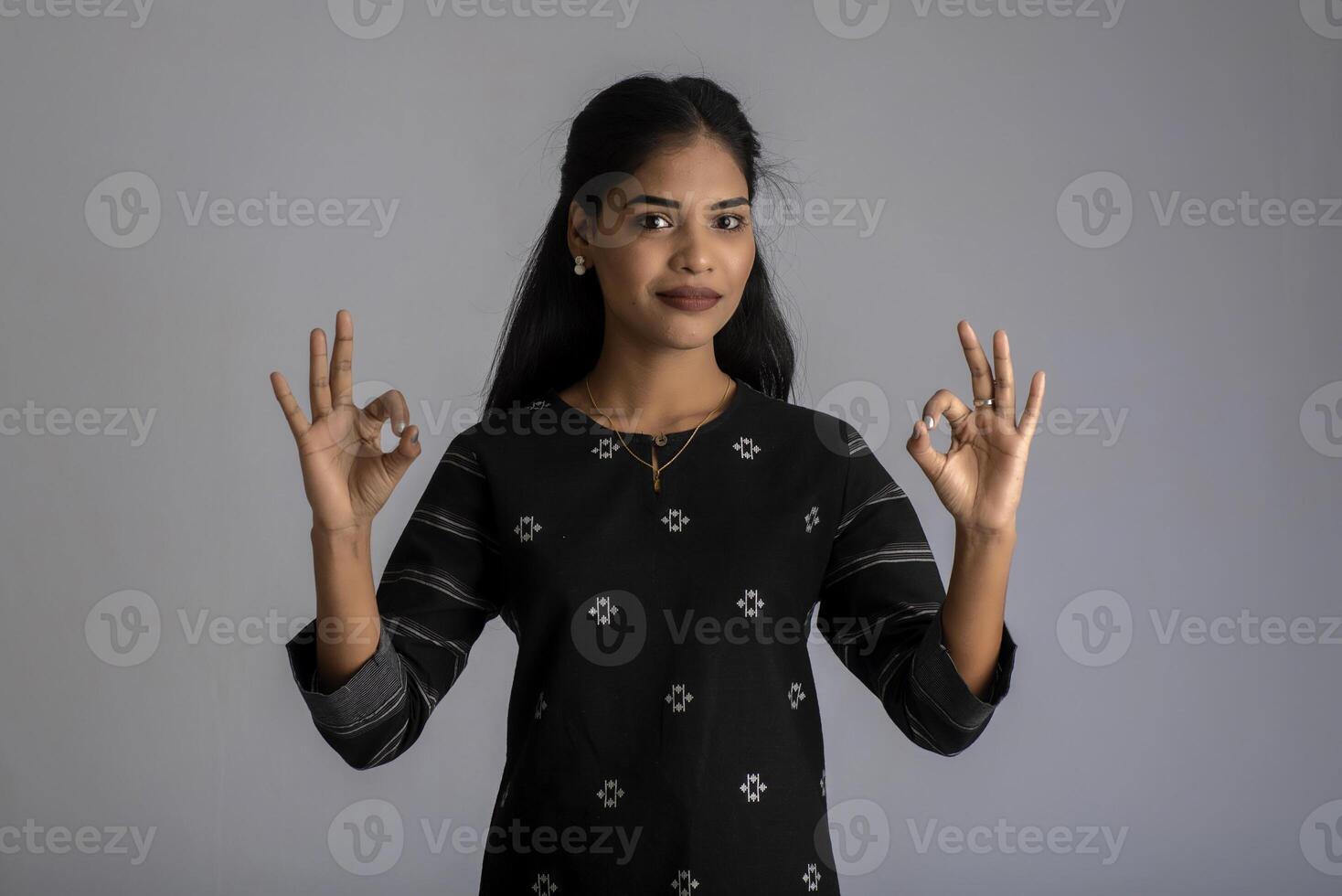 Young smiling girl showing ok sign or thumbs up on a grey background photo