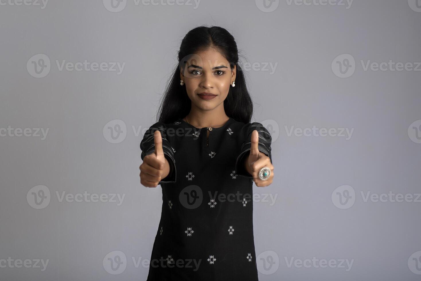 Young smiling girl showing ok sign or thumbs up on a grey background photo