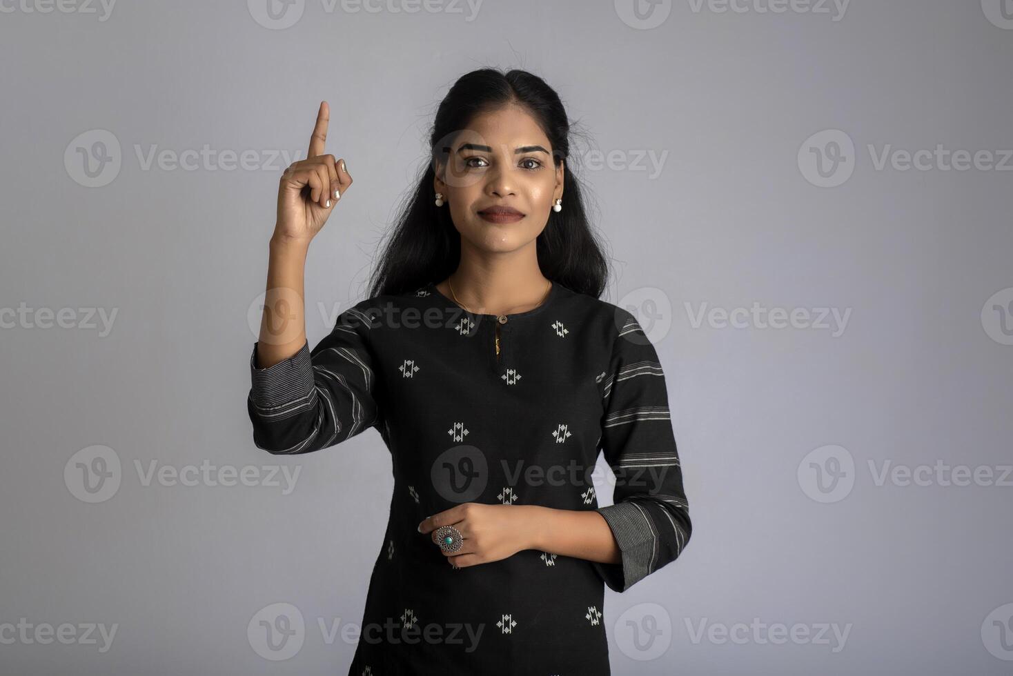 Young smiling girl pointing fingers to copy space on a grey background photo