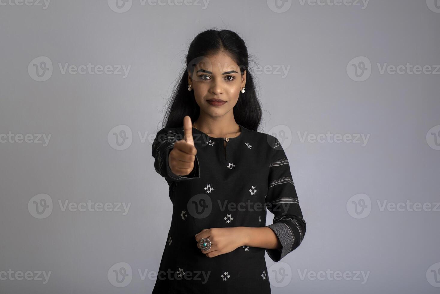 Young smiling girl showing ok sign or thumbs up on a grey background photo