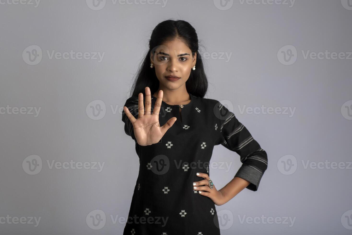 Portrait of a beautiful girl showing stop sign on a grey background photo