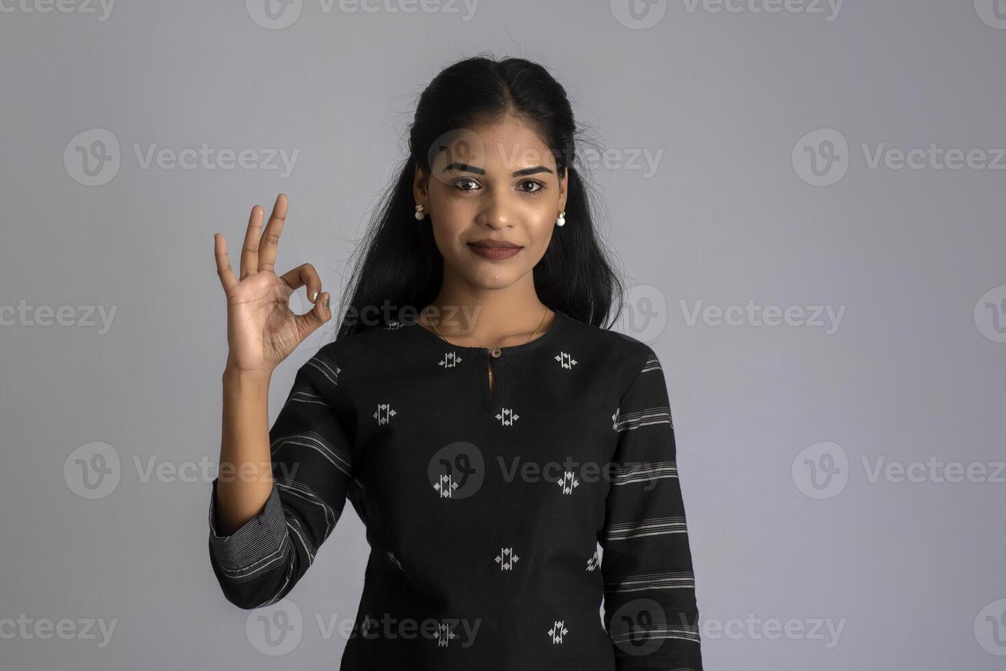 Young smiling girl showing ok sign or thumbs up on a grey background photo