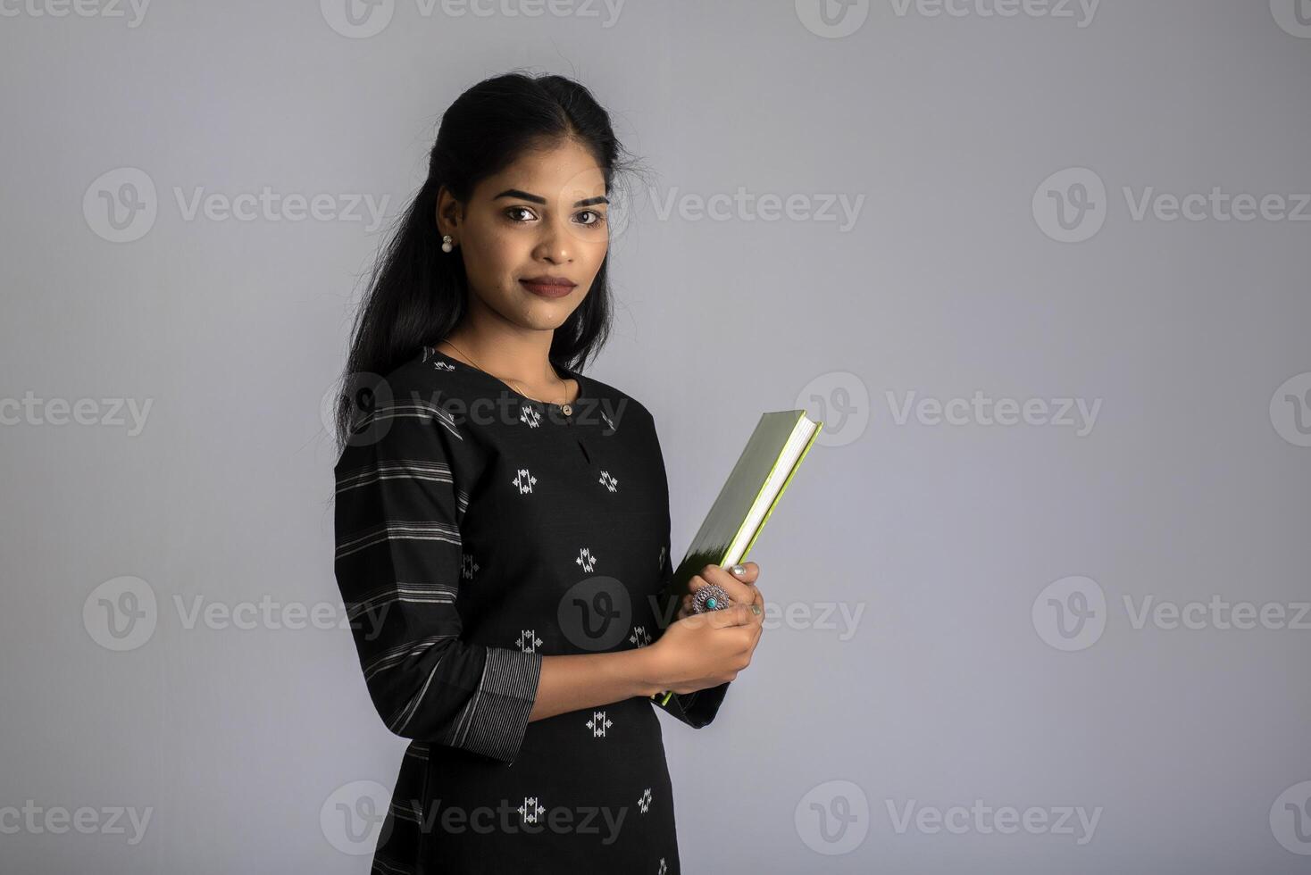Pretty young girl holding book and posing on grey background photo