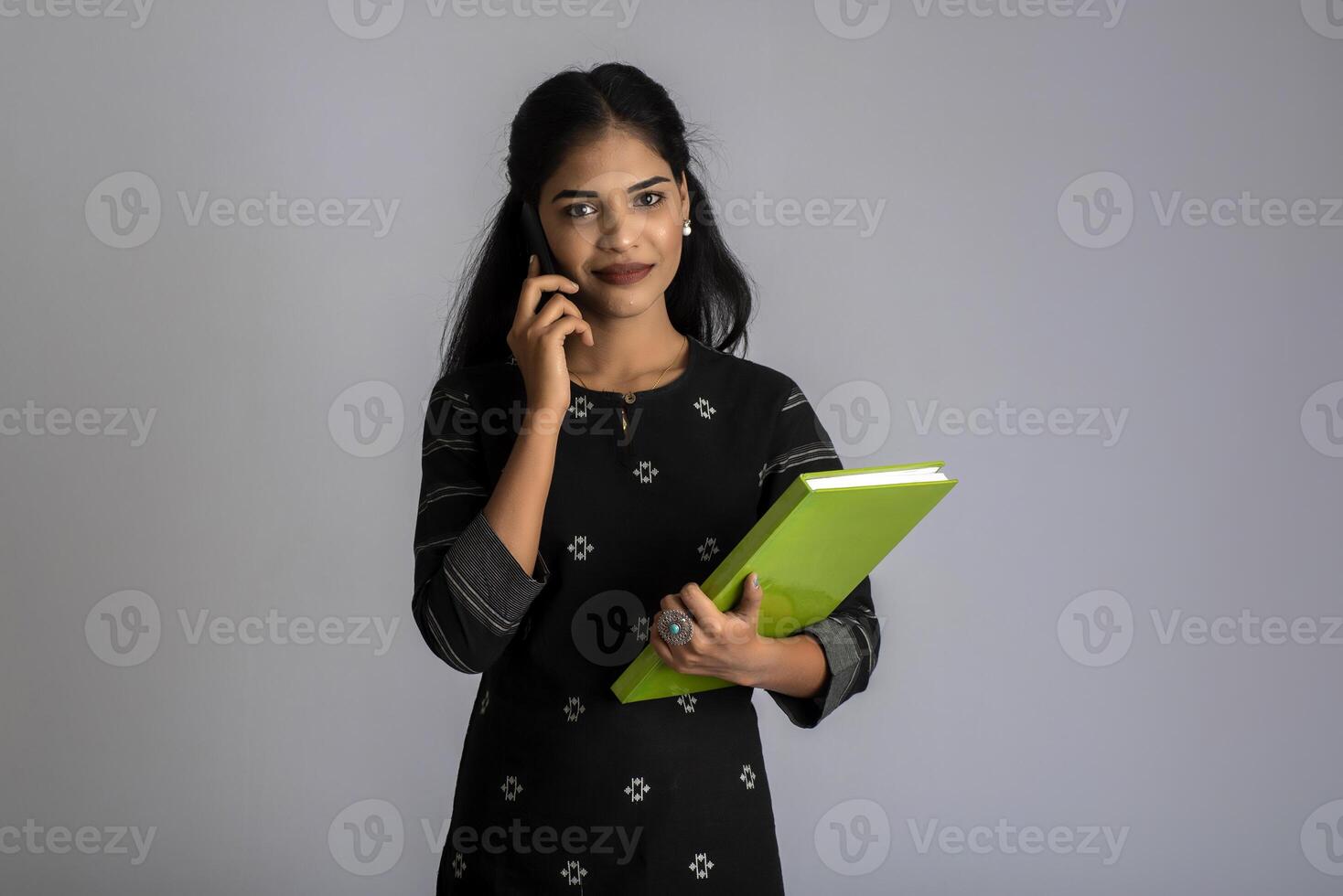Pretty young girl holding book and using mobile on grey background photo