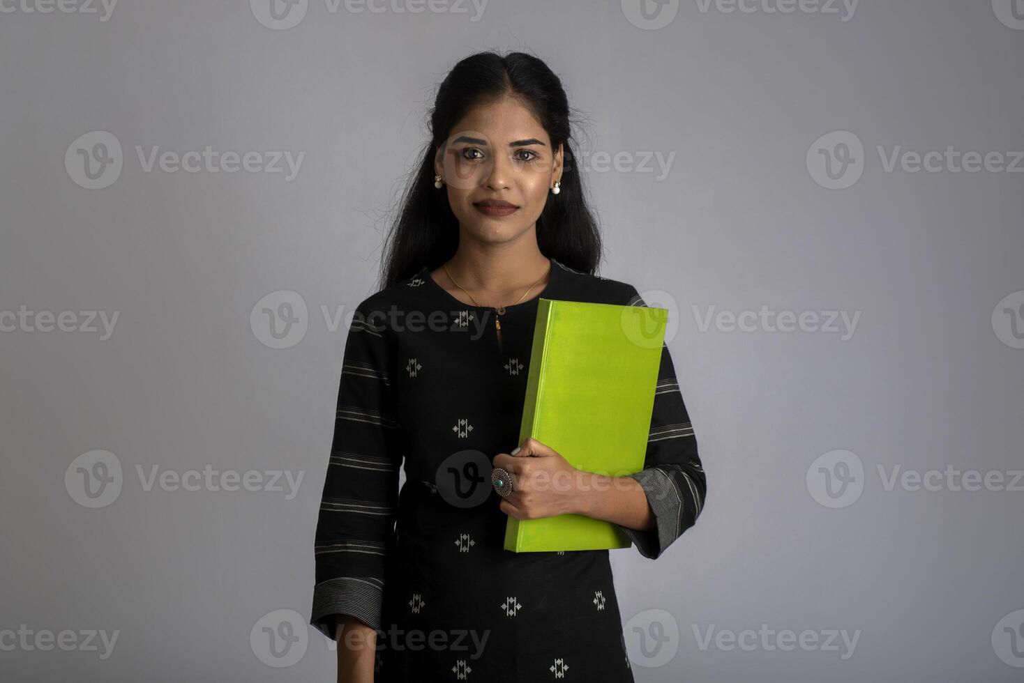 Pretty young girl holding book and posing on grey background photo