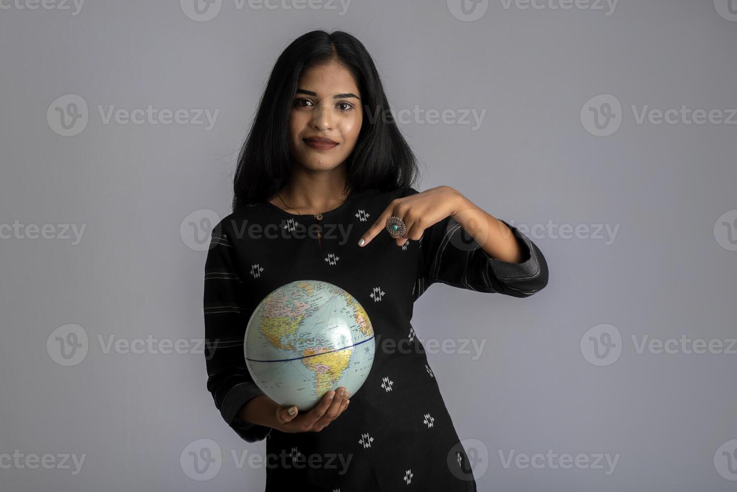 young girl holding the world globe and posing on a grey background. photo