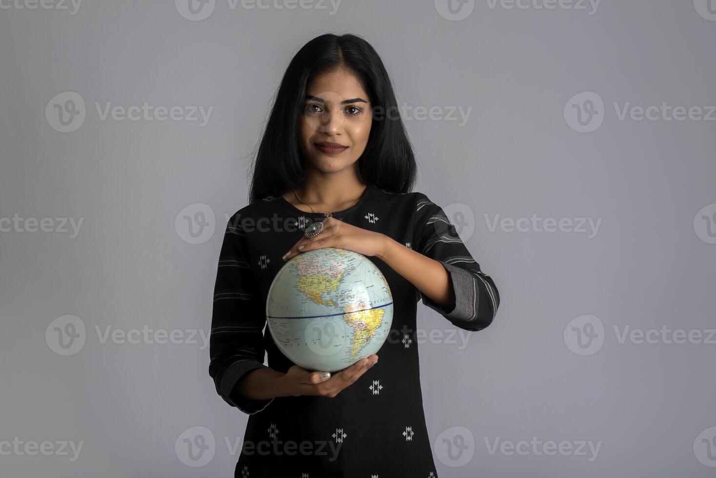 young girl holding the world globe and posing on a grey background. photo