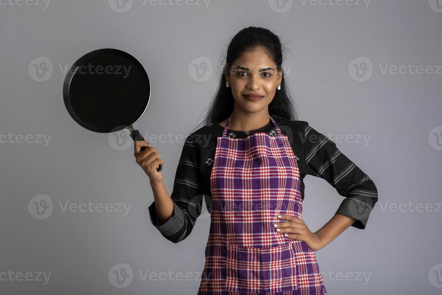 Young girl holding kitchen utensils spatula and pan on a grey background photo