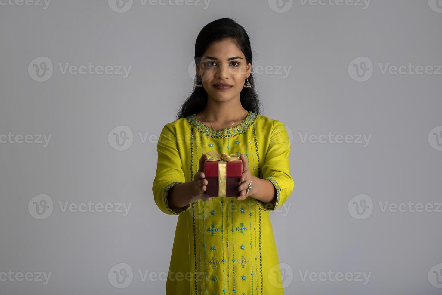 Portrait of young happy smiling woman Girl holding gift box on a grey background. photo