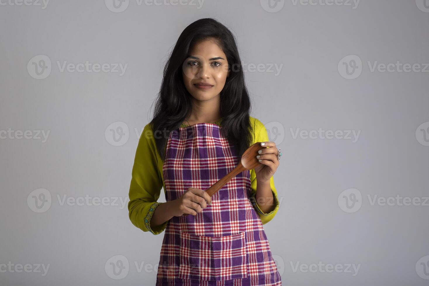 Young girl holding and posing with kitchen utensils spatula on a grey background photo