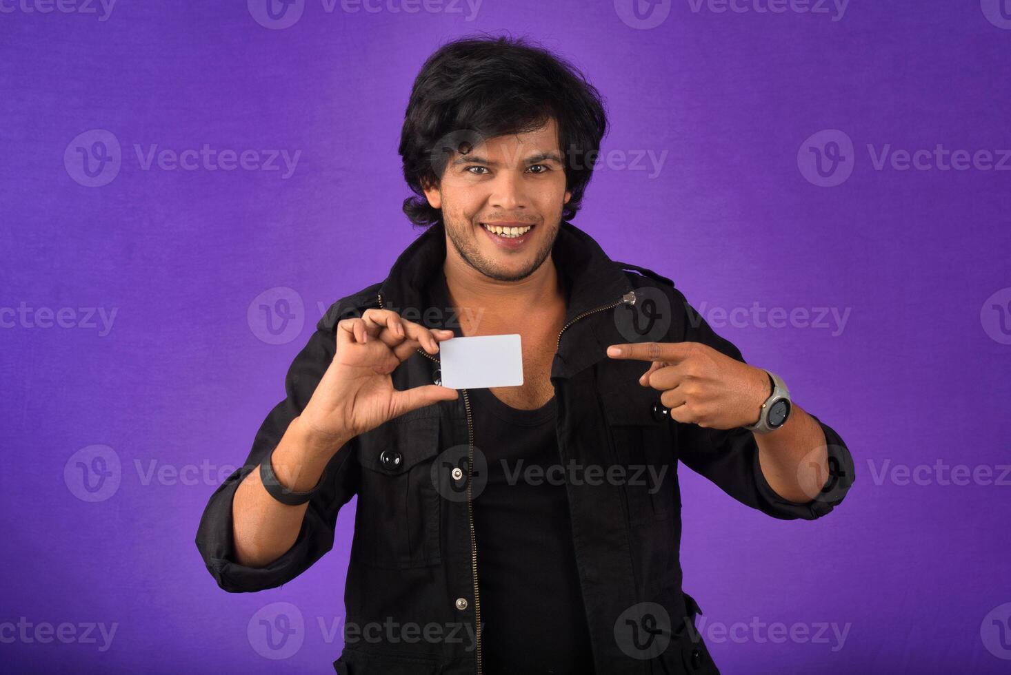 Young smiling handsome man posing with a credit card on purple background. photo