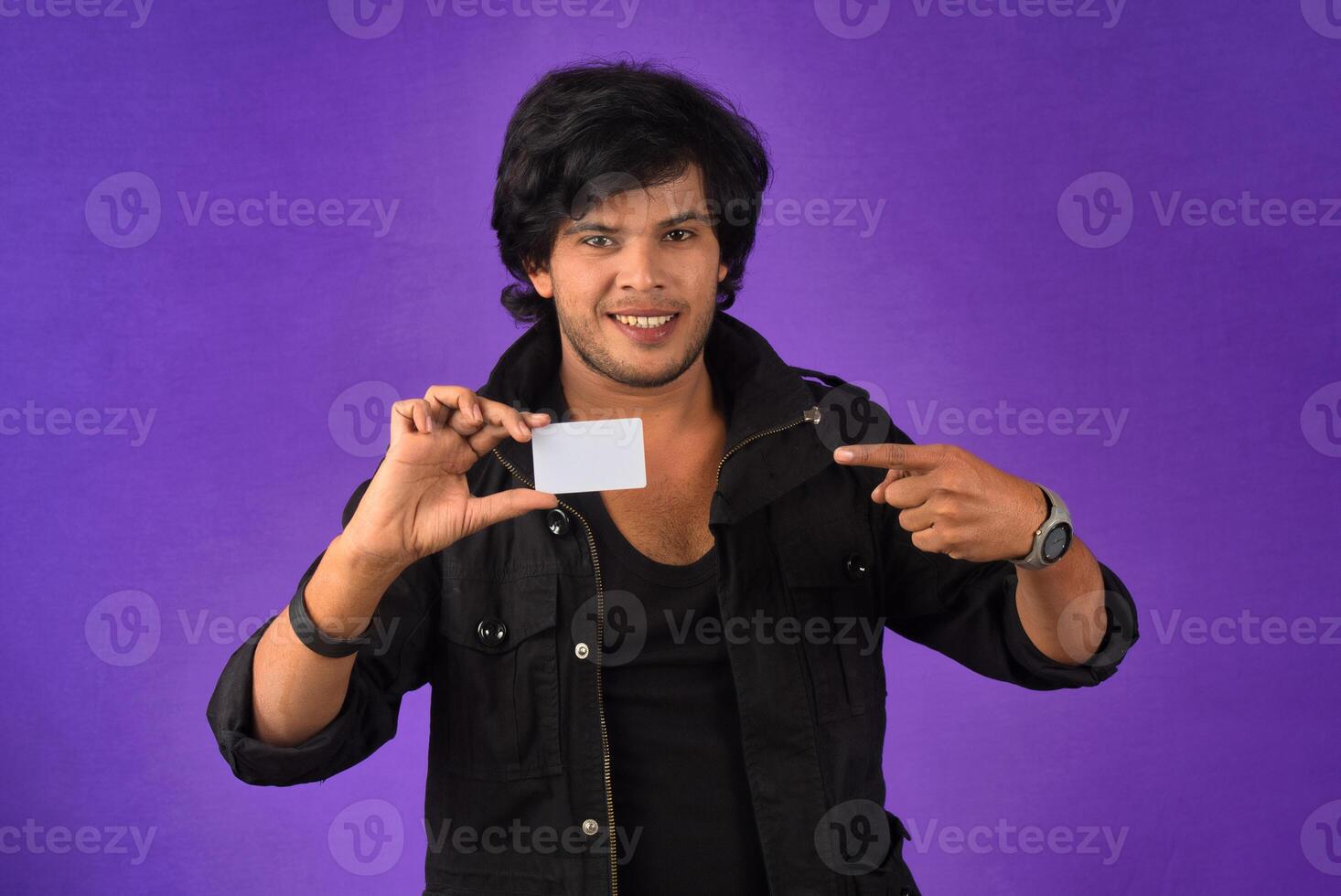 Young smiling handsome man posing with a credit card on purple background. photo