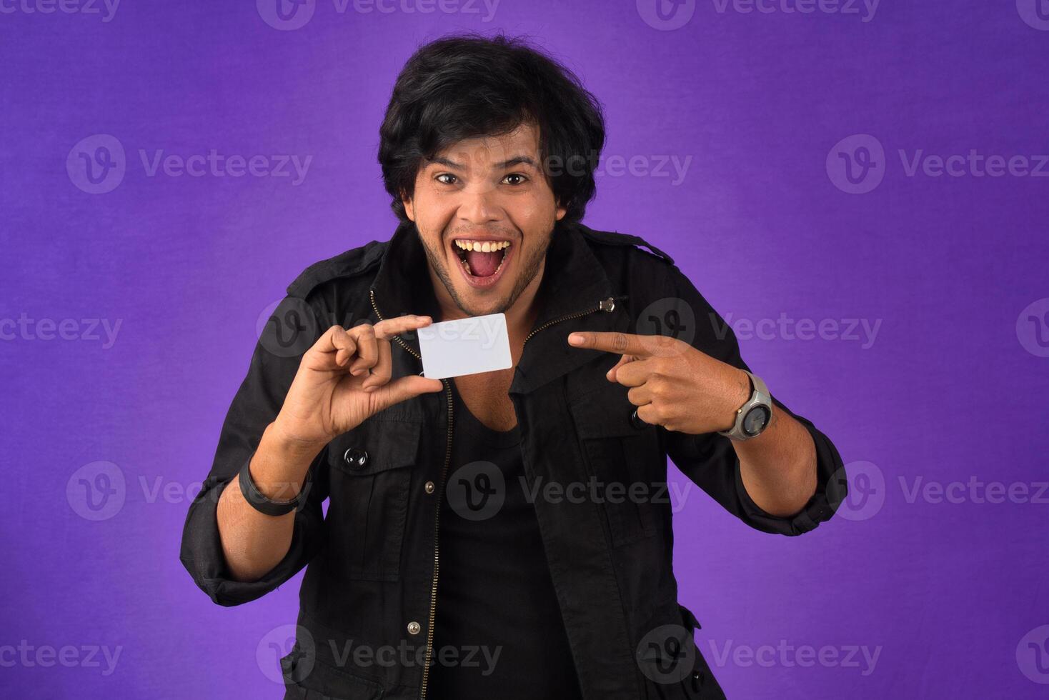 Young smiling handsome man posing with a credit card on purple background. photo