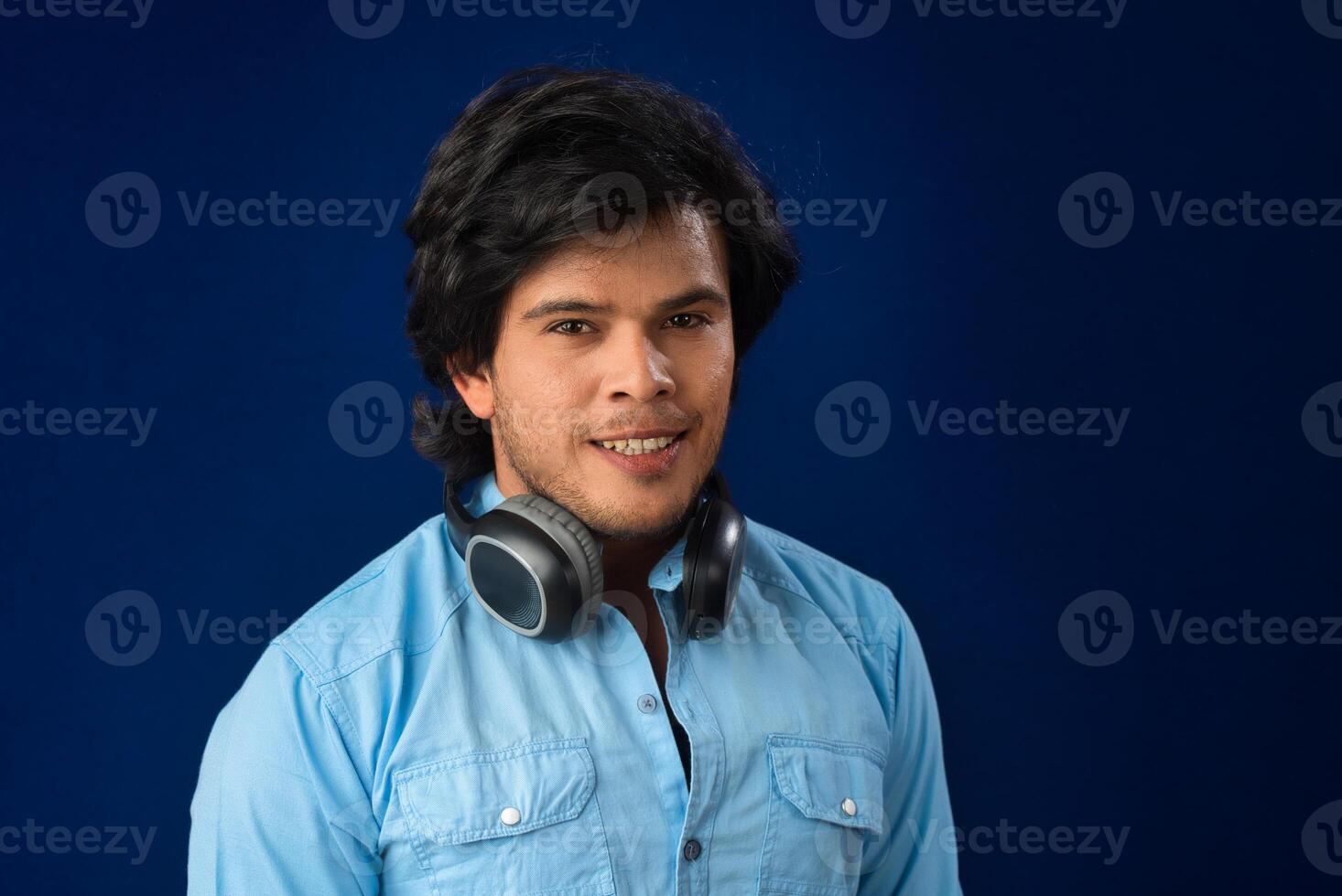 Portrait of a handsome young man enjoying music on headphones on blue background. photo