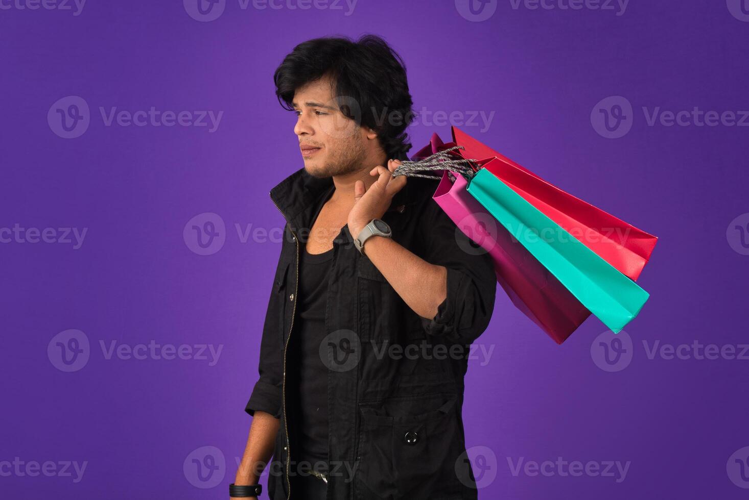 Beautiful Indian young handsome man holding and posing with shopping bags on a purple background photo