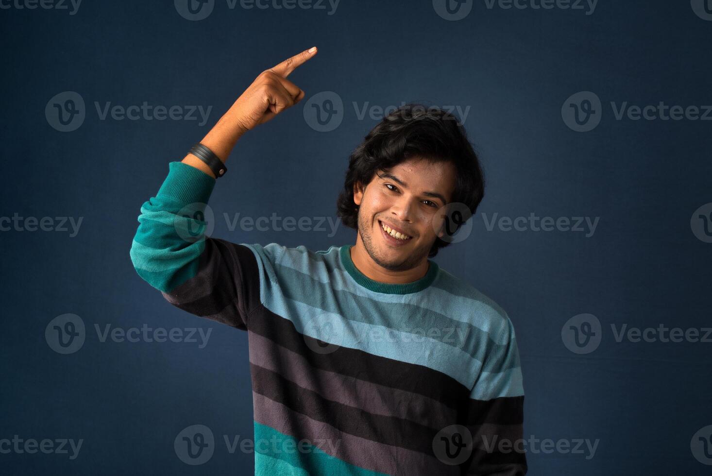 Portrait of a successful cheerful young man pointing and presenting something with hand or finger with a happy smiling face. photo