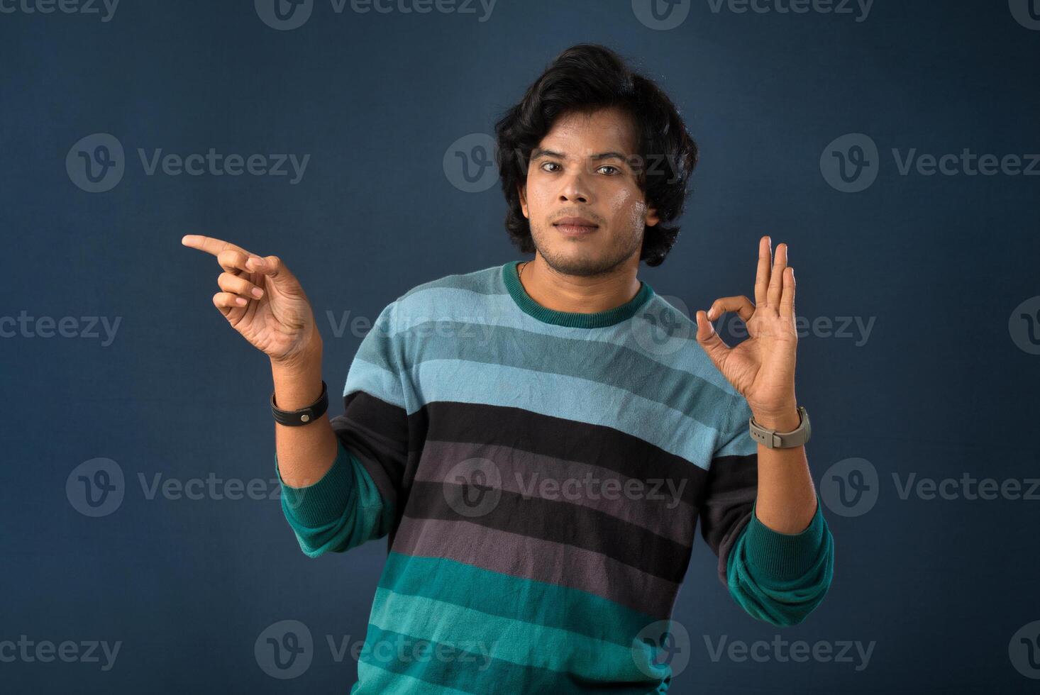 Portrait of a successful cheerful young man pointing and presenting something with hand or finger with a happy smiling face. photo