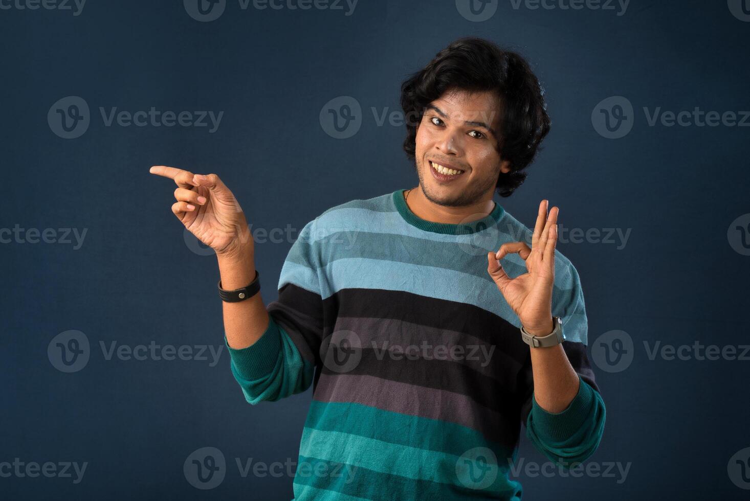 Portrait of a successful cheerful young man pointing and presenting something with hand or finger with a happy smiling face. photo