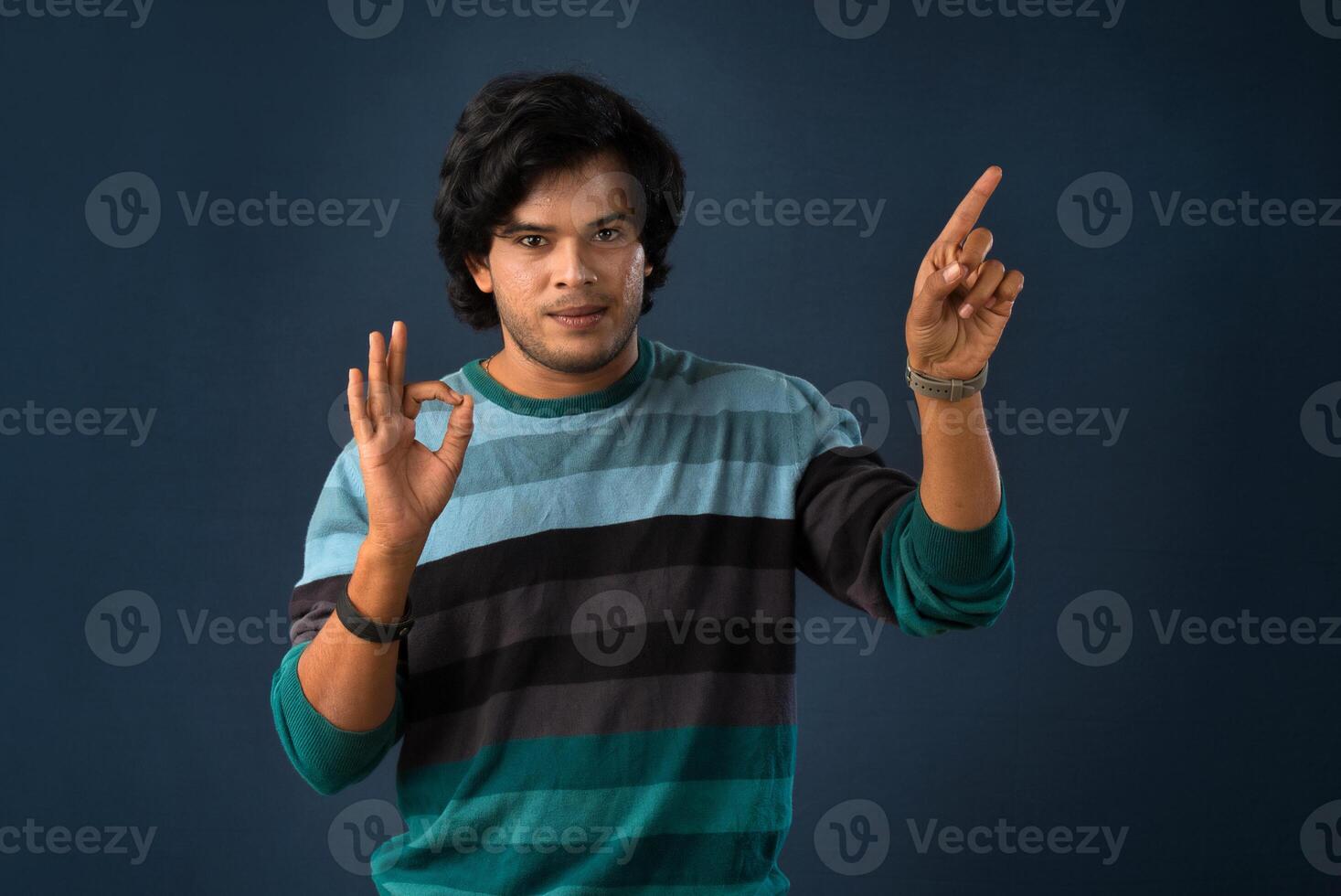 Portrait of a successful cheerful young man pointing and presenting something with hand or finger with a happy smiling face. photo