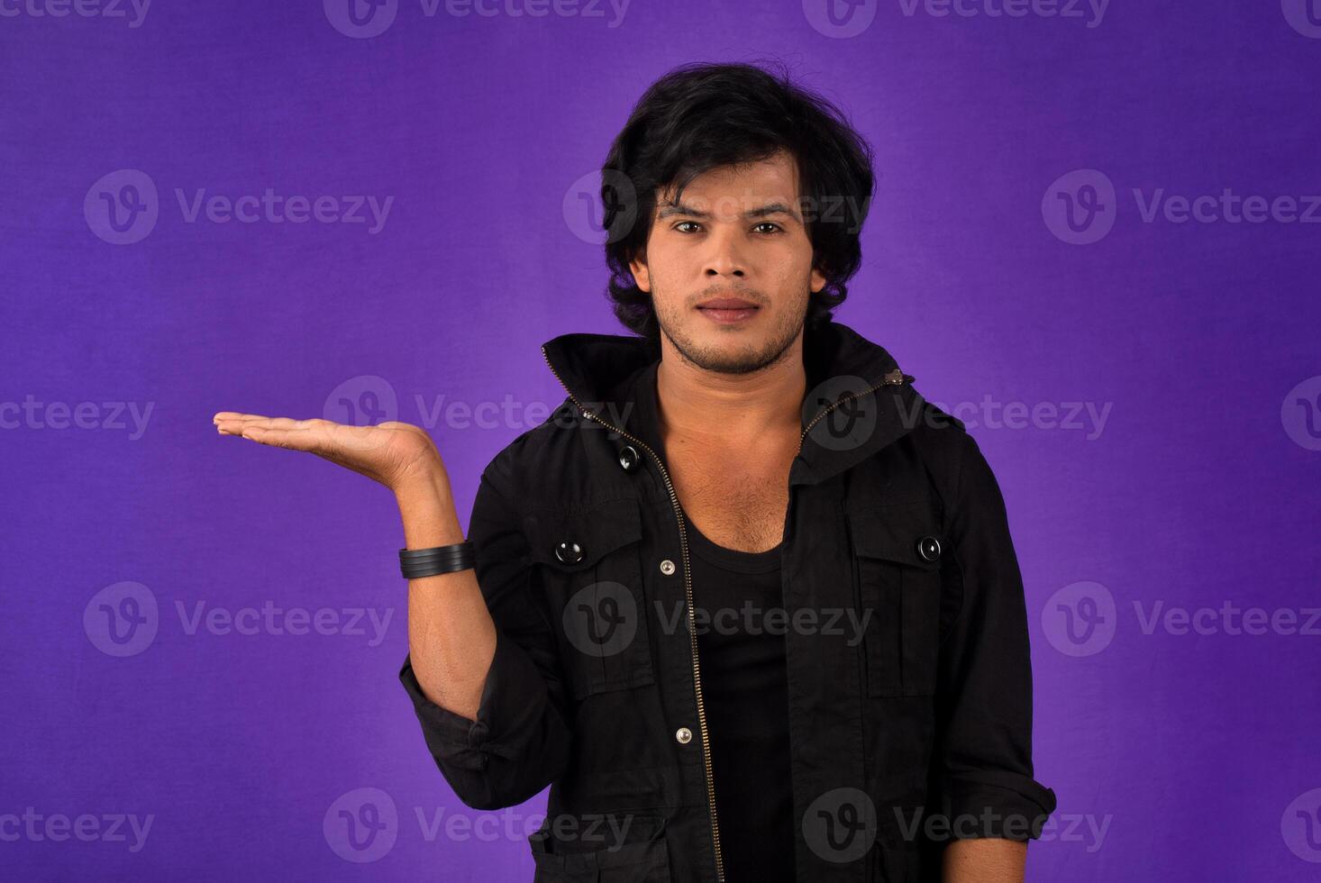Portrait of a successful cheerful young man holding and presenting something on hand with a happy smiling face. photo