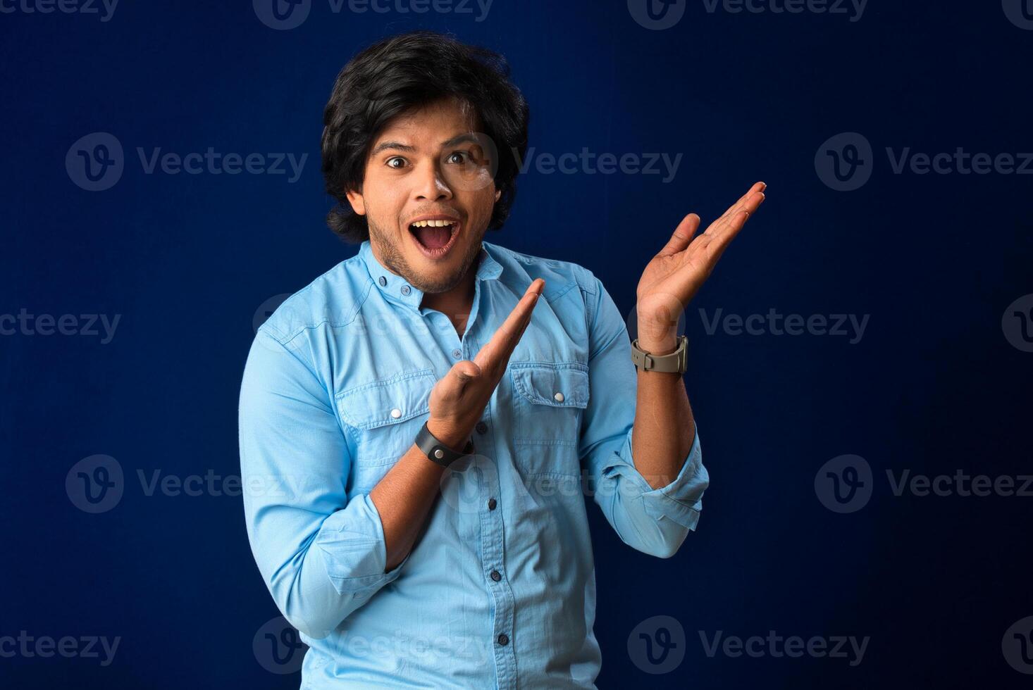 Portrait of a successful cheerful young man pointing and presenting something with hand or finger with a happy smiling face. photo