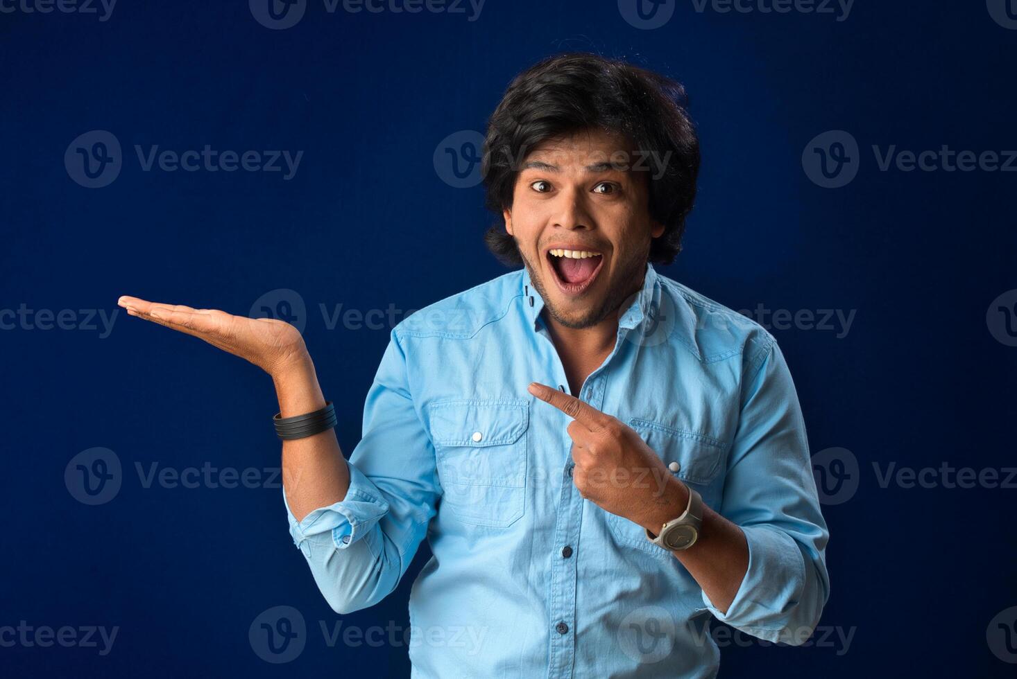 Portrait of a successful cheerful young man holding and presenting something on hand with a happy smiling face. photo