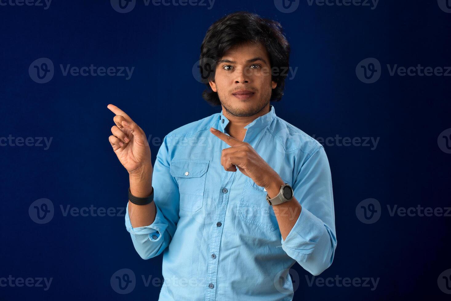 Portrait of a successful cheerful young man pointing and presenting something with hand or finger with a happy smiling face. photo